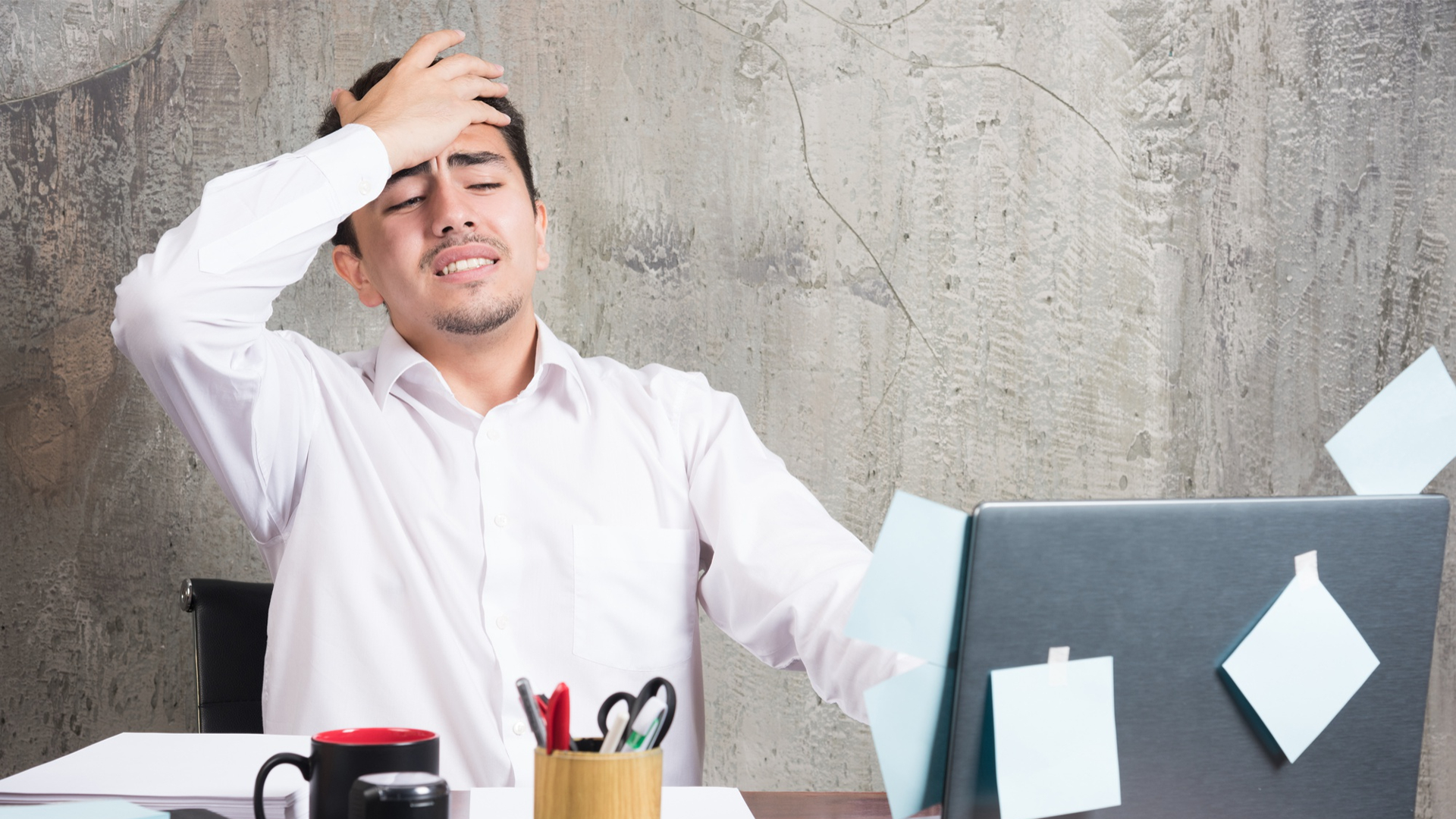 A man in a white with headache position, laptop, sticky note