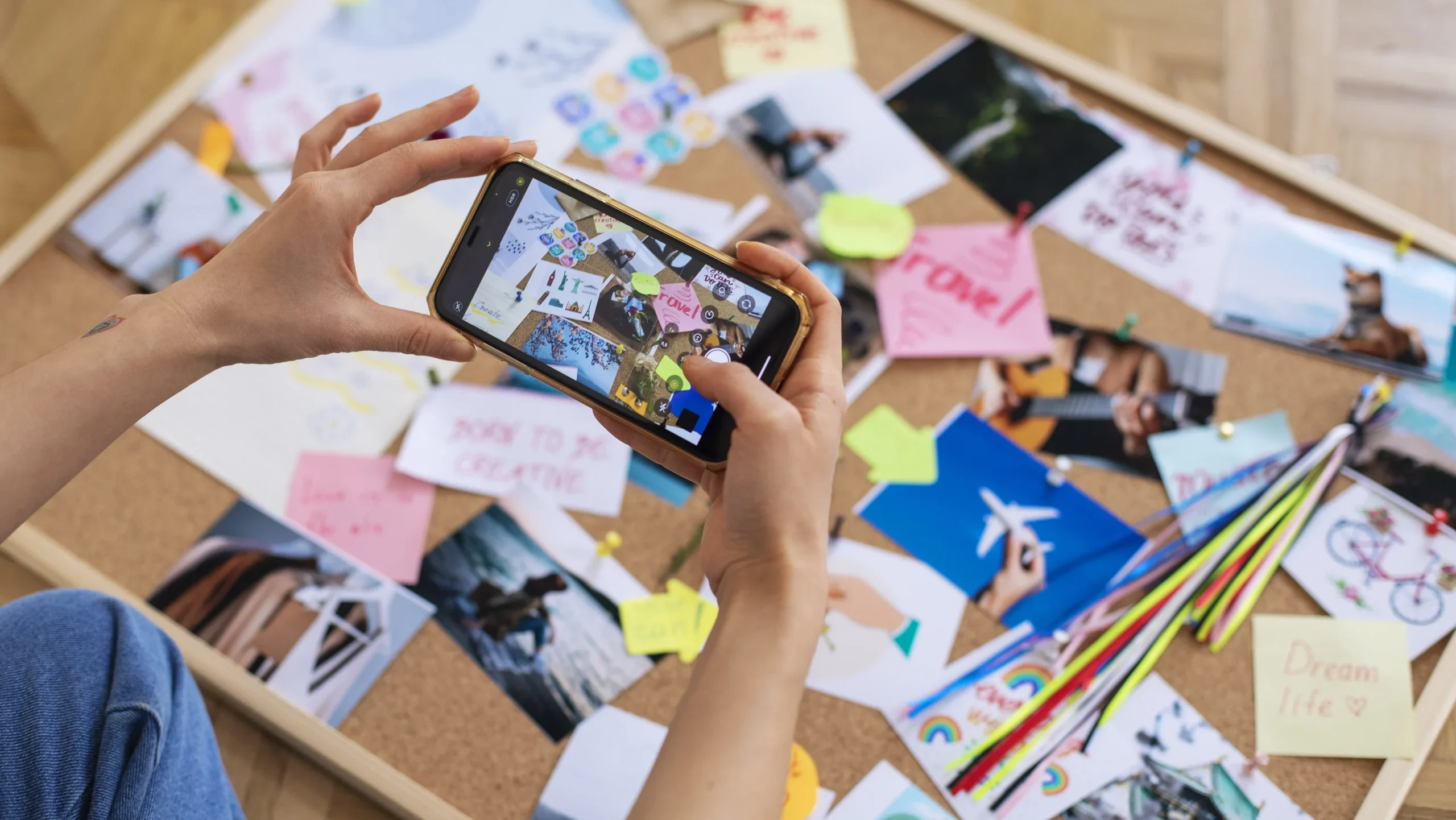 Person taking a photo of a colorful vision board with inspiring notes, photos, and drawings, symbolizing creativity and goal planning.