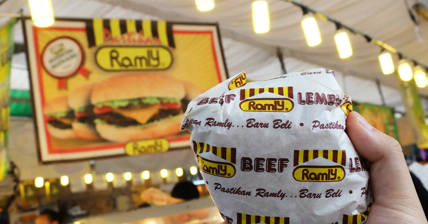 Burger Ramly dibungkus di gerai burger dengan banner Ramly di belakang