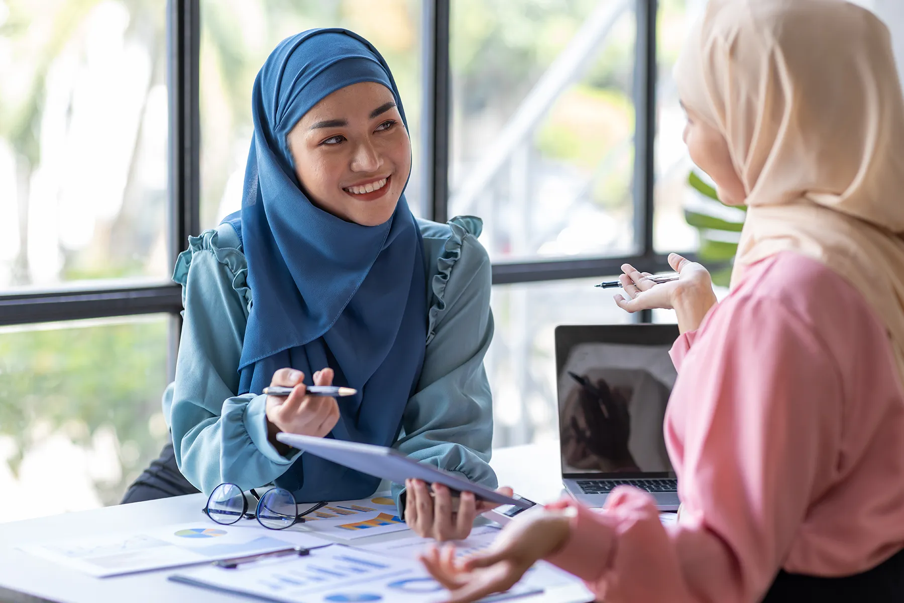 Two Muslim women discussing work documents in an office setting