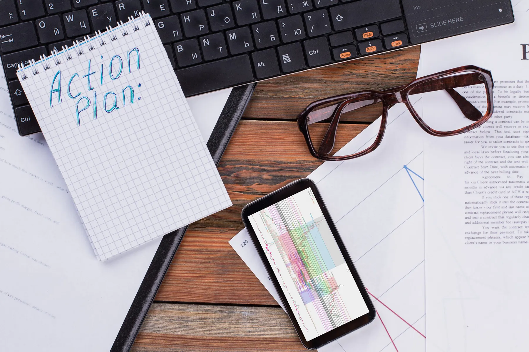 Action plan notebook on desk with phone showing analytics and paperwork