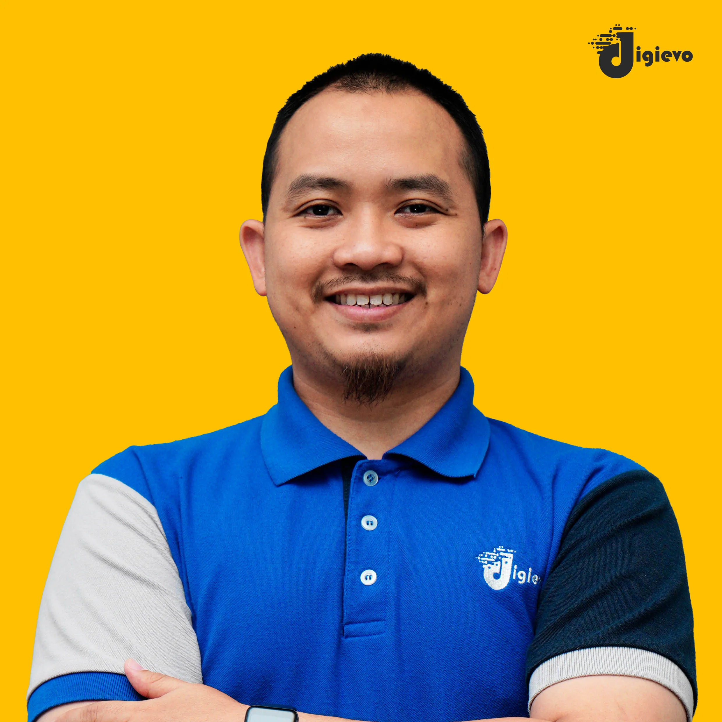 Lelaki tersenyum memakai baju polo biru, tangan bersilang, dengan latar kuning.