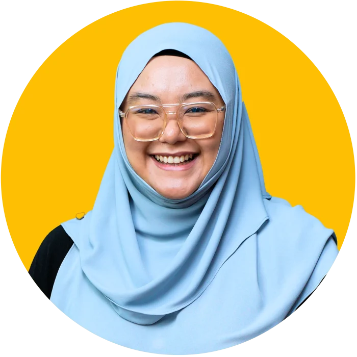 Wanita berhijab biru muda tersenyum dalam foto potret berlatar belakang kuning.