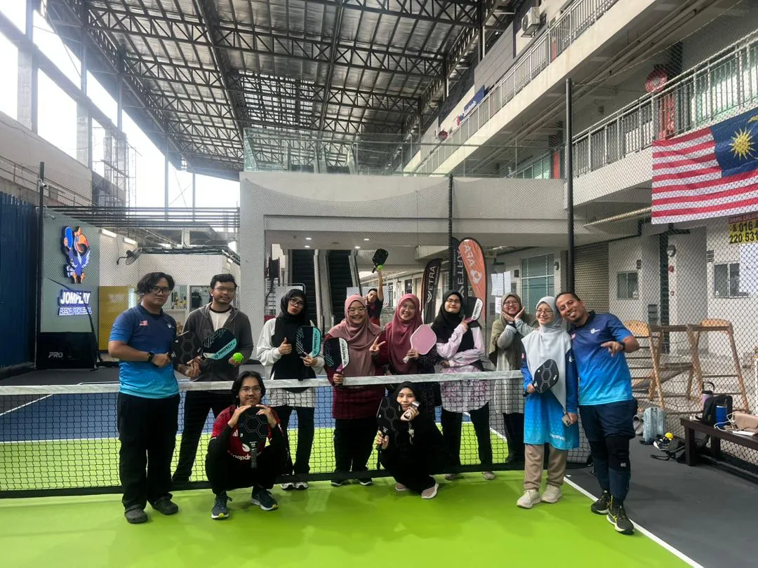 Kumpulan peserta bermain pickleball di gelanggang indoor sambil bergambar dengan raket