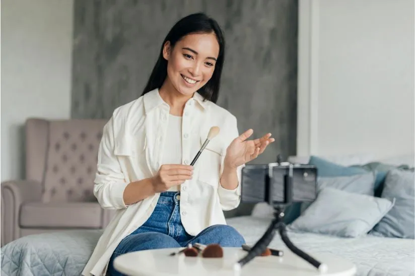 Beauty vlogger filming a makeup tutorial at home using a smartphone camera.